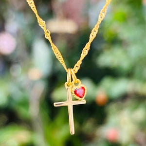 Op de afbeelding: Een gouden ketting met een klein gouden kruisje en een rode hartvormige hanger.