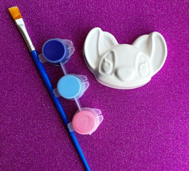 May include: A white ceramic figurine shaped like a cartoon dog with three paint pots: blue, light blue, and pink.