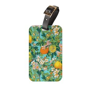 May include: A turquoise luggage tag with a black leather strap and a gold buckle. The tag features a repeating pattern of lemons, oranges, and white flowers on a turquoise background.