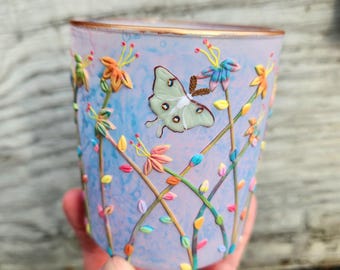 Pequeña polilla luna fosforescente y flores silvestres arcoíris esculpidas con arcilla polimérica sobre un portavelas de vidrio reciclado.