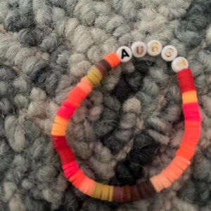 May include: A colorful beaded bracelet with the word "AUGUST" spelled out in white letters on white beads.