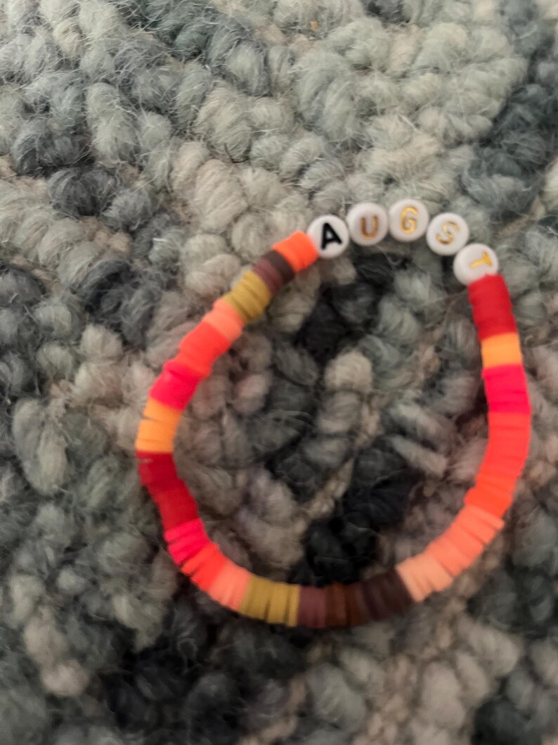 May include: A colorful beaded bracelet with the word "AUGUST" spelled out in white letters on white beads.