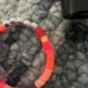 May include: A colorful beaded bracelet with red, orange, yellow, brown, and white beads.