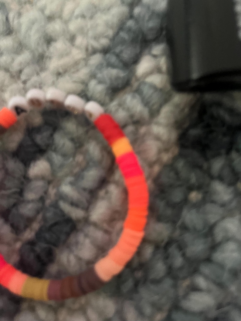 May include: A colorful beaded bracelet with red, orange, yellow, brown, and white beads.