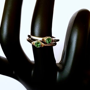Puede incluir: Dos anillos de plata con piedras preciosas verdes engastadas en el centro de cada anillo. Los anillos están apilados uno encima del otro.