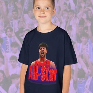 Pode incluir: Camiseta azul marinho com um jogador de basquete e o texto vermelho "All-Star". O jogador está vestindo uma camisa vermelha e está com a boca aberta. O fundo mostra uma multidão de pessoas.