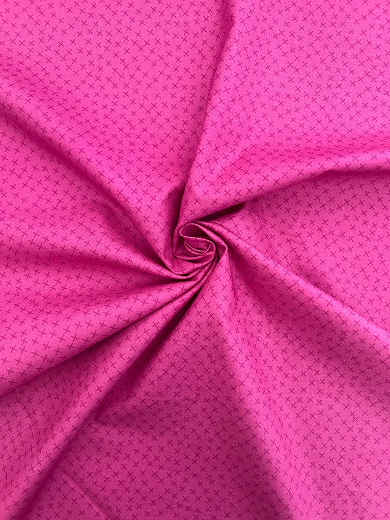 May include: A close-up of a pink fabric with a subtle crosshatch pattern. The fabric is folded and draped, showcasing its texture and color.