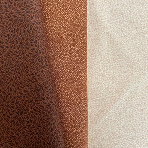 Könnte beinhalten: Drei Stoffmuster mit unterschiedlichen Mustern. Das linke Muster ist braun mit einem dunkelbraunen Blatt-Muster. Das mittlere Muster ist braun mit einem hellbraunen Punkt-Muster. Das rechte Muster ist hellbraun mit einem weißen Punkt-Muster.