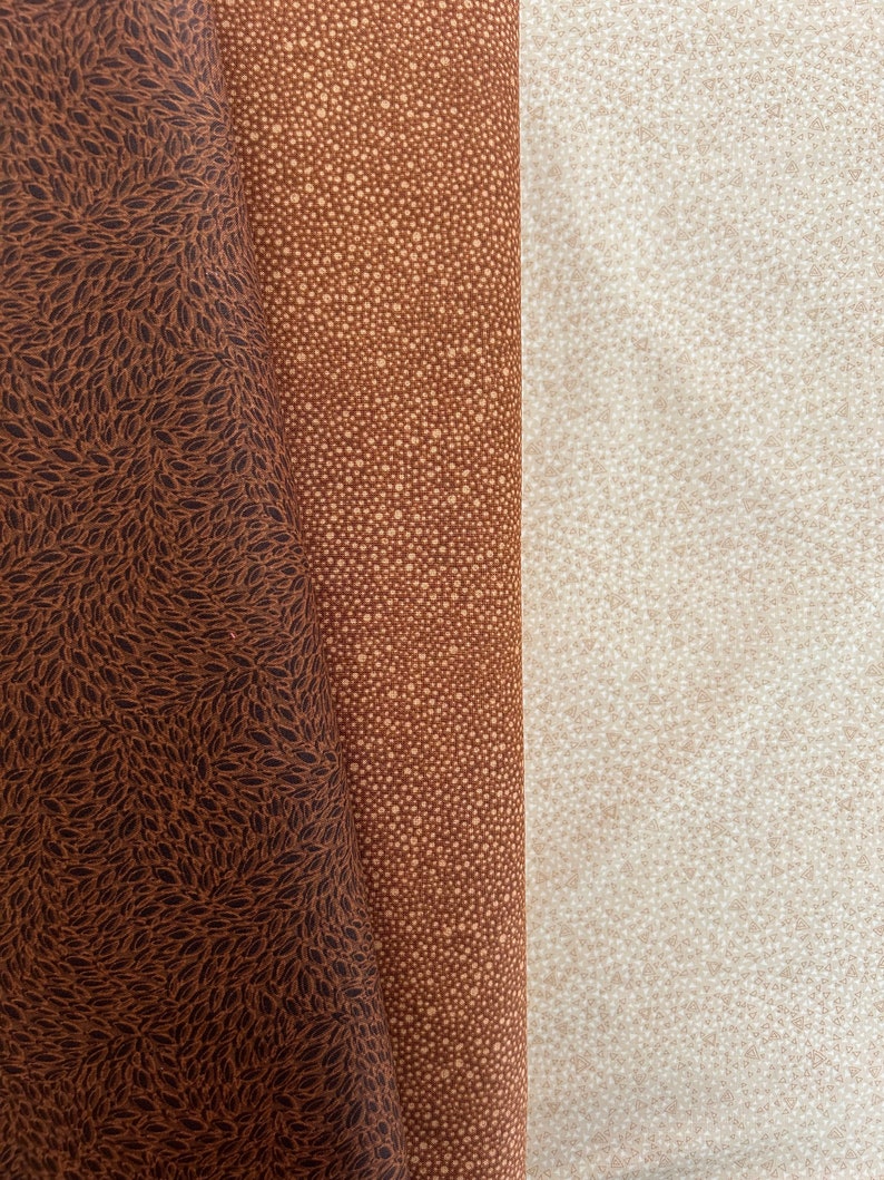 May include: Three fabric swatches with different patterns. The left swatch is brown with a dark brown leaf pattern. The middle swatch is brown with a light brown dot pattern. The right swatch is light brown with a white dot pattern.