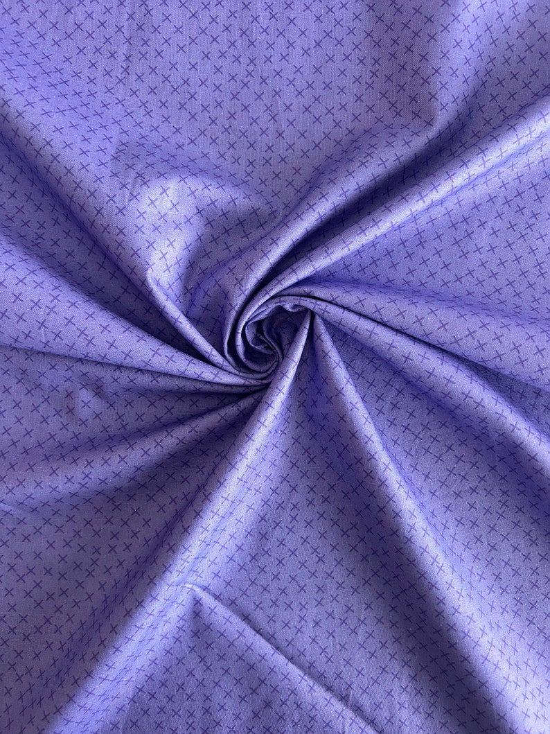 May include: A close-up of a purple fabric with a subtle crosshatch pattern. The fabric is folded and draped, showcasing its texture and drape.