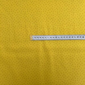 Puede incluir: Una tela amarilla con un patr&oacute;n repetitivo de peque&ntilde;as cruces marrones oscuras. Una regla se coloca sobre la tela, mostrando medidas en cent&iacute;metros.