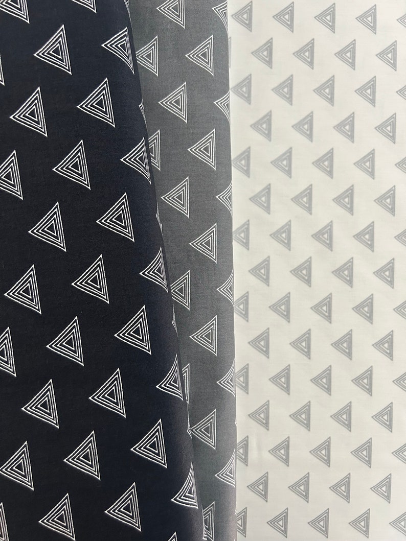 Puede incluir: Dos muestras de tela con un patr&oacute;n geom&eacute;trico de tri&aacute;ngulos conc&eacute;ntricos blancos sobre un fondo negro y gris.