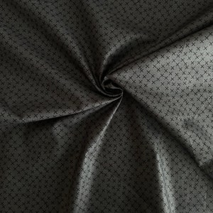 May include: A close-up of a dark gray fabric with a repeating pattern of small black crosses.