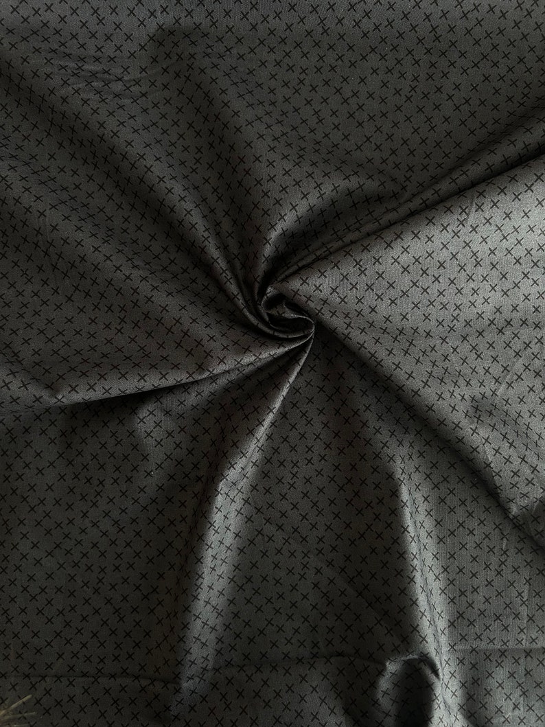May include: A close-up of a dark gray fabric with a repeating pattern of small black crosses.