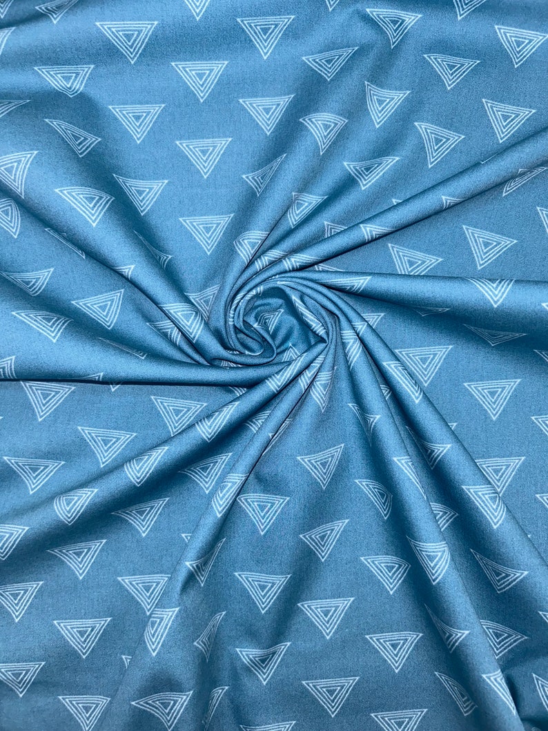 May include: A close-up shot of blue fabric with a repeating pattern of white, nested triangles. The fabric is gathered and folded, creating a swirling effect. The triangles are evenly spaced across the material.