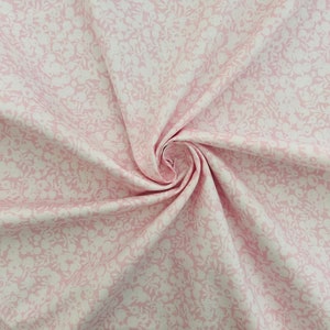 Może przedstawiać: R&oacute;żowy materiał z białym wzorem kwiatowym. Materiał jest złożony i skręcony, co ukazuje fakturę i wz&oacute;r.