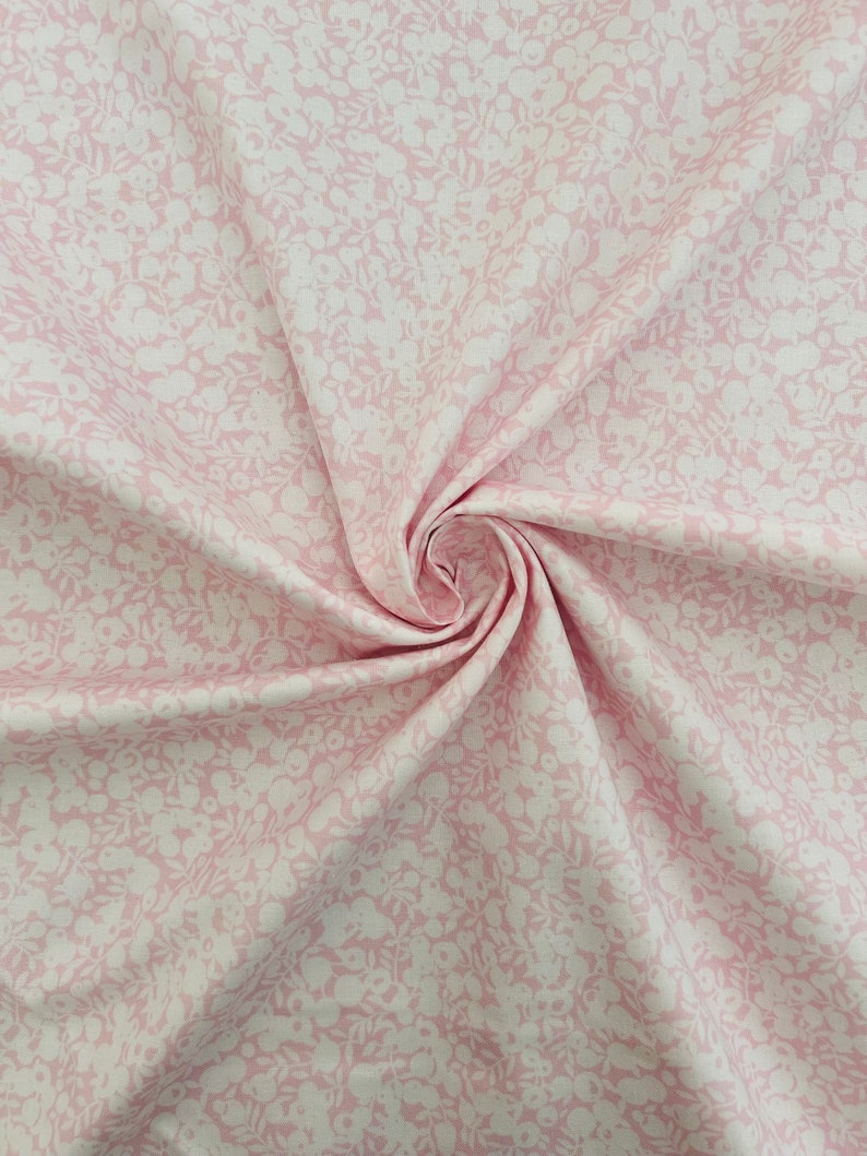 Może przedstawiać: R&oacute;żowy materiał z białym wzorem kwiatowym. Materiał jest złożony i skręcony, co ukazuje fakturę i wz&oacute;r.