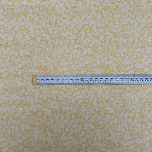 Pu&ograve; includere: Primo piano di un tessuto giallo con un motivo floreale bianco. Un righello &egrave; visibile nella parte inferiore dell'immagine.