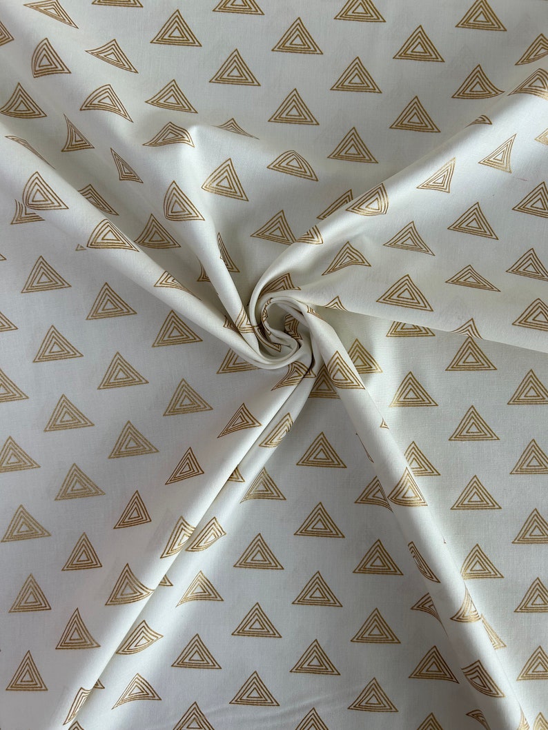 Puede incluir: Tela blanca con un patr&oacute;n repetitivo de tri&aacute;ngulos dorados. Los tri&aacute;ngulos est&aacute;n formados por l&iacute;neas conc&eacute;ntricas.