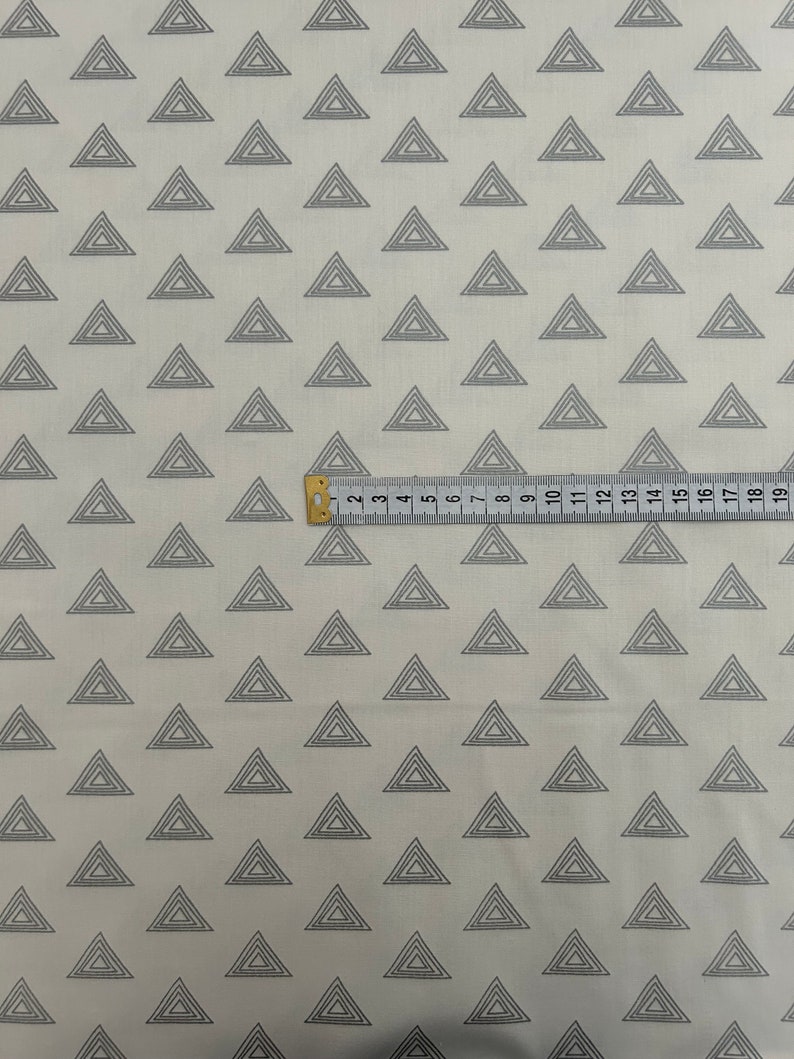 Puede incluir: Tela blanca con un patr&oacute;n repetido de tri&aacute;ngulos conc&eacute;ntricos grises. Una regla se coloca sobre la tela, mostrando medidas en pulgadas.