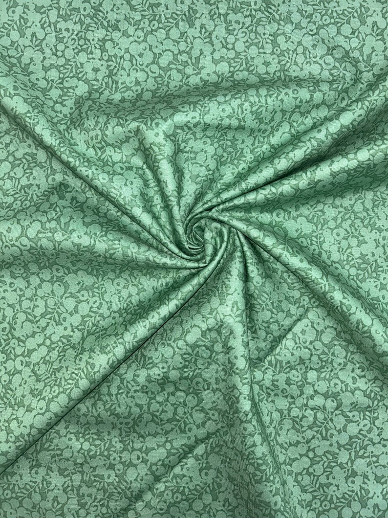 Pu&ograve; includere: Un primo piano di un tessuto verde con un motivo floreale bianco. Il tessuto &egrave; piegato e ha una consistenza morbida e testurizzata.