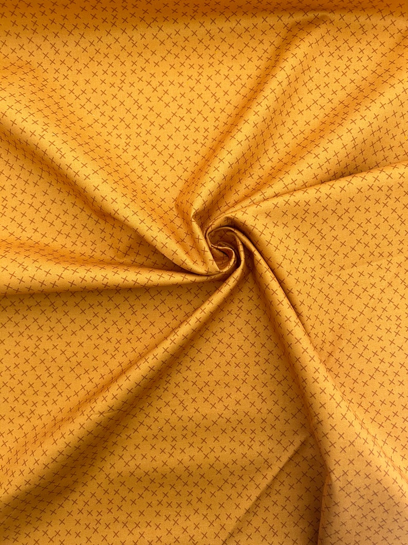 Puede incluir: Primer plano de una tela amarilla con un patr&oacute;n repetitivo de peque&ntilde;as cruces rojas. La tela est&aacute; doblada y drapeada, mostrando su textura.