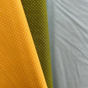 Könnte beinhalten: Drei Stoffmuster mit weißen Punkten auf verschiedenen farbigen Hintergründen. Die Muster sind gelb, grün und hellblau.