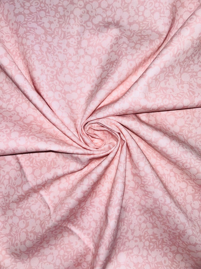 Może przedstawiać: R&oacute;żowy materiał z białym wzorem kwiatowym. Materiał jest złożony i skręcony, co ukazuje jego fakturę i wz&oacute;r.