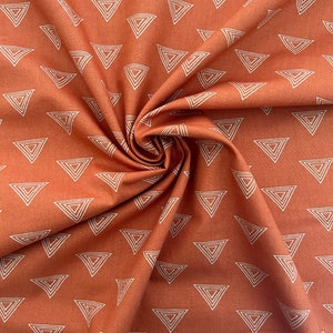 Puede incluir: Una tela de color &oacute;xido con un patr&oacute;n geom&eacute;trico blanco de tri&aacute;ngulos. La tela est&aacute; doblada y drapeada, mostrando el patr&oacute;n.