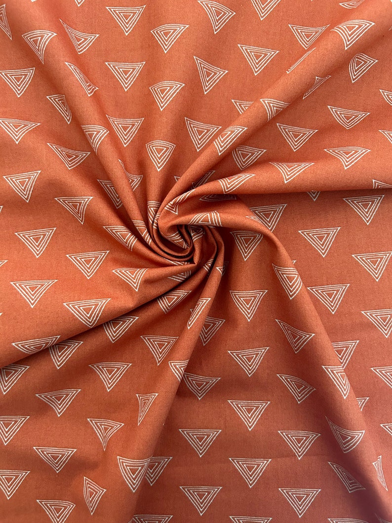 Puede incluir: Una tela de color &oacute;xido con un patr&oacute;n geom&eacute;trico blanco de tri&aacute;ngulos. La tela est&aacute; doblada y drapeada, mostrando el patr&oacute;n.