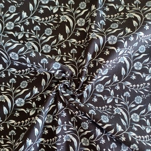 Könnte beinhalten: Schwarzer Stoff mit weißem Blumenmuster. Der Stoff zeigt ein sich wiederholendes Muster aus kleinen weißen Blüten und Blättern.