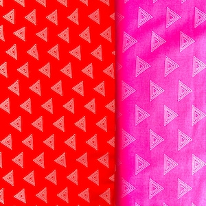 Könnte beinhalten: Zwei Stoffbahnen, eine rote und eine rosa, werden gezeigt. Beide Bahnen weisen ein sich wiederholendes Muster aus weiß umrandeten Dreiecken auf. Die rote Bahn befindet sich links, die rosa Bahn rechts, teilweise gefaltet.