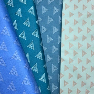 Könnte beinhalten: Vier Stoffmuster in Blautönen und einem hellen Pfirsichton. Jedes Muster zeigt ein sich wiederholendes Muster aus weißen oder pfirsichfarbenen verschachtelten Dreiecken. Die Stoffe sind gefaltet und zeigen die Textur und Farbvariationen.