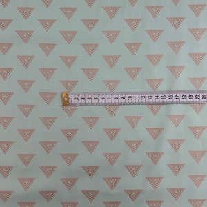 May include: Light blue fabric with a repeating pattern of nested, light brown triangles. A yellow and white measuring tape is laid across the fabric, showing measurements up to 21 inches.