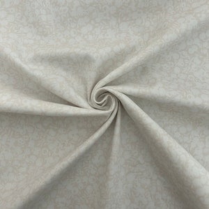 Może przedstawiać: Zbliżenie beżowego materiału z subtelnym białym wzorem kwiatowym. Materiał jest złożony i ma miękką, fakturowaną powierzchnię.