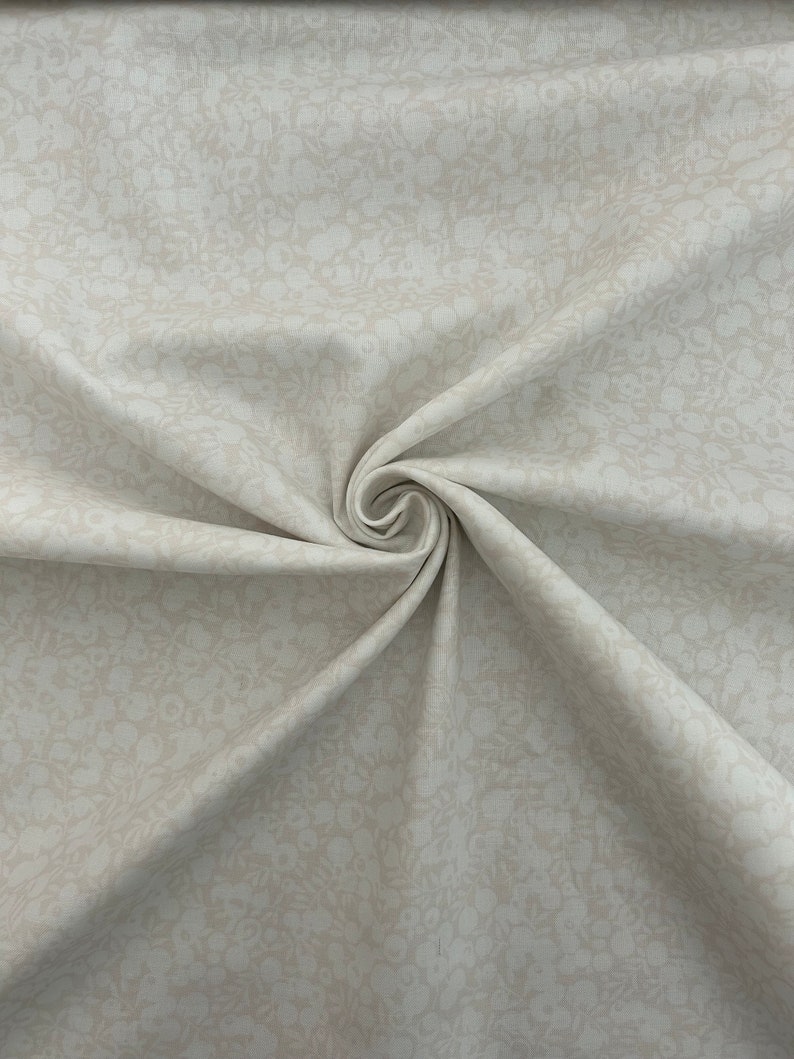 Może przedstawiać: Zbliżenie beżowego materiału z subtelnym białym wzorem kwiatowym. Materiał jest złożony i ma miękką, fakturowaną powierzchnię.