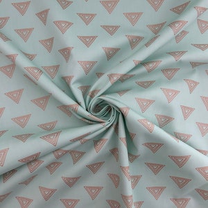 May include: A light blue fabric with a repeating pattern of brown outlined triangles. The triangles are arranged in a scattered layout across the fabric. The fabric is folded and draped, showing the texture and flow of the material.