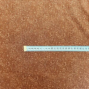 May include: Brown fabric with a white polka dot pattern. The fabric is measured with a ruler that shows inches.