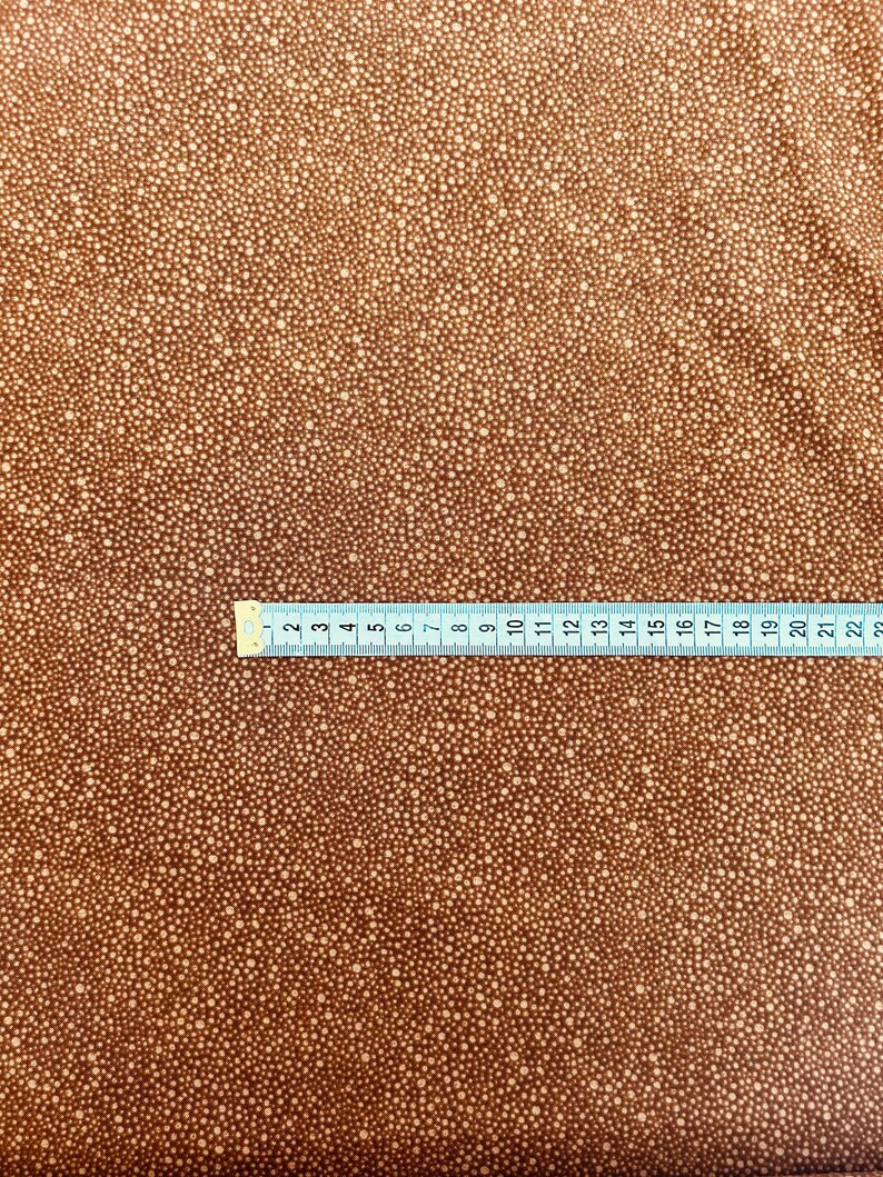 May include: Brown fabric with a white polka dot pattern. The fabric is measured with a ruler that shows inches.