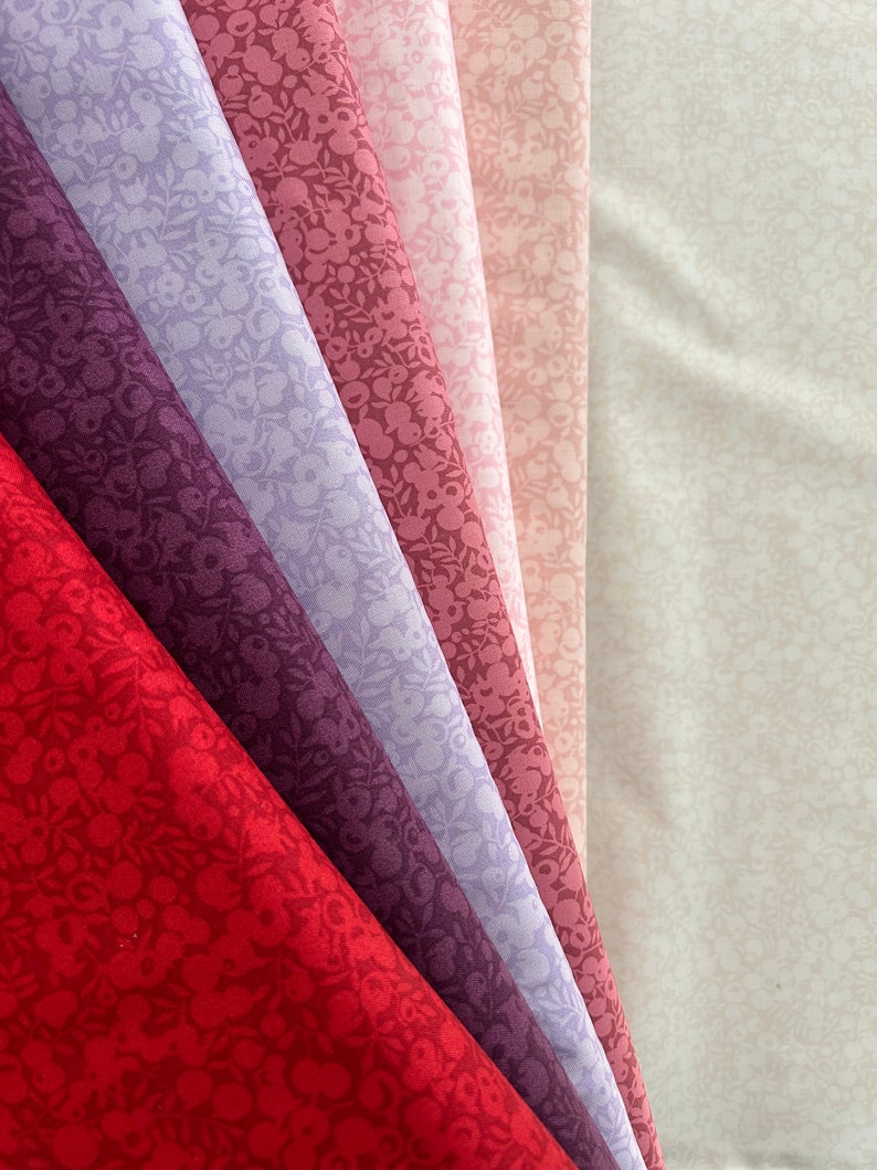 Może przedstawiać: Kolekcja sześciu pr&oacute;bek tkaniny w r&oacute;żnych odcieniach r&oacute;żu i fioletu z małym wzorem kwiatowym. Pr&oacute;bki są ułożone wachlarzowo, z najjaśniejszym odcieniem na g&oacute;rze i najciemniejszym odcieniem na dole.