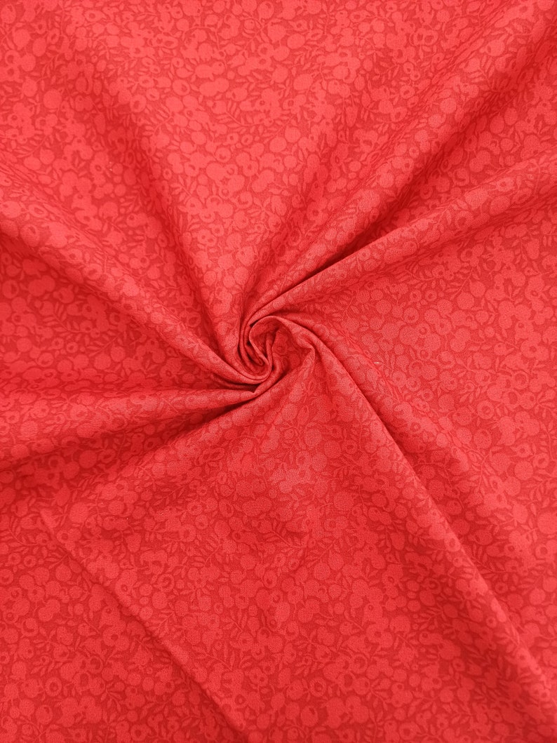 Może przedstawiać: Czerwony materiał z małym białym wzorem kwiatowym. Materiał jest złożony i ma miękką, fakturowaną fakturę.