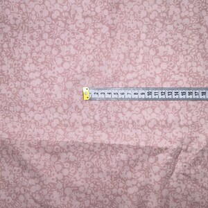 Może przedstawiać: Zbliżenie na r&oacute;żowy materiał z białym wzorem kwiatowym. Na materiale leży miarka, pokazująca wymiary w calach.