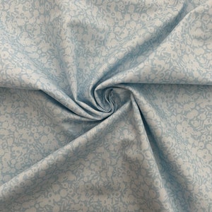 Pu&ograve; includere: Un tessuto blu chiaro con un motivo floreale bianco. Il tessuto &egrave; piegato e ha una consistenza morbida.