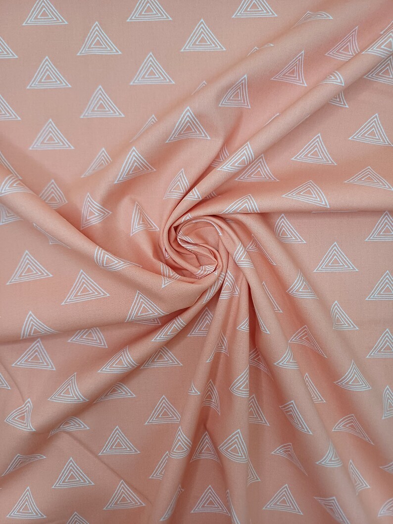 Puede incluir: Tela de color melocot&oacute;n con un patr&oacute;n geom&eacute;trico blanco de tri&aacute;ngulos repetidos. La tela est&aacute; doblada y drapeada, mostrando la textura y el patr&oacute;n.