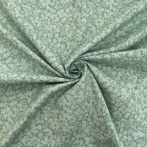 Pu&ograve; includere: Un tessuto verde salvia con un motivo floreale bianco. Il tessuto &egrave; piegato e ha una superficie morbida e testurizzata.