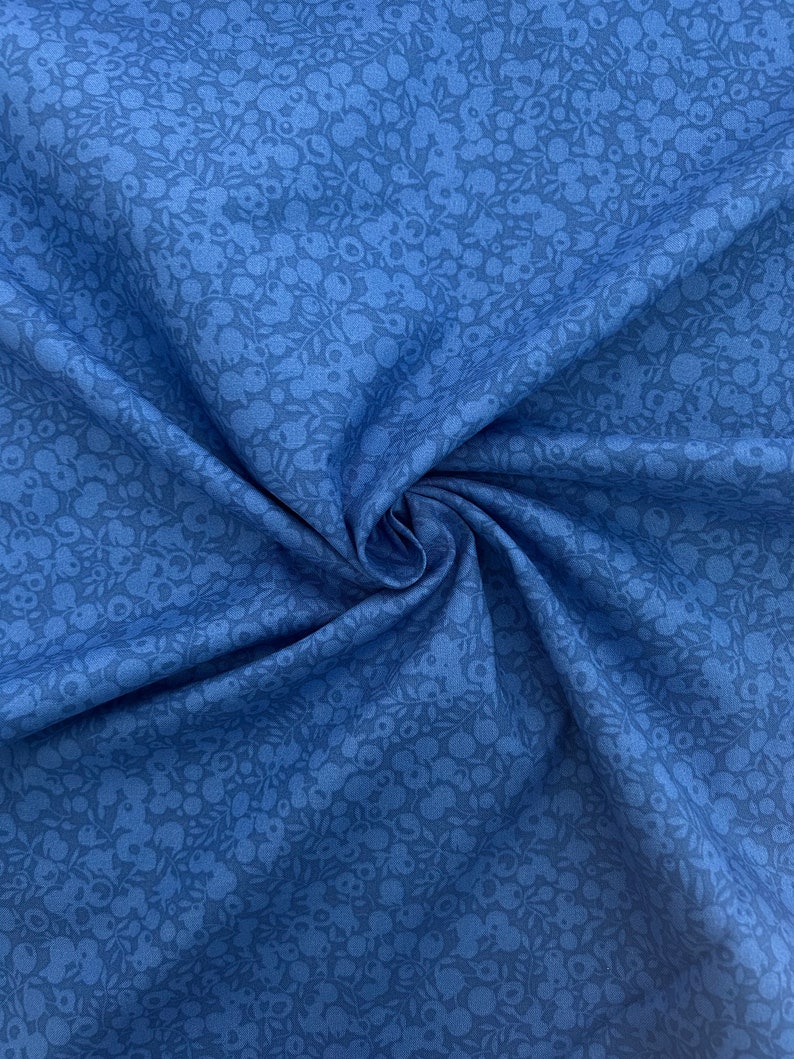 Pu&ograve; includere: Un primo piano di un tessuto blu con un motivo floreale bianco. Il tessuto &egrave; morbido e ha una lucentezza sottile.