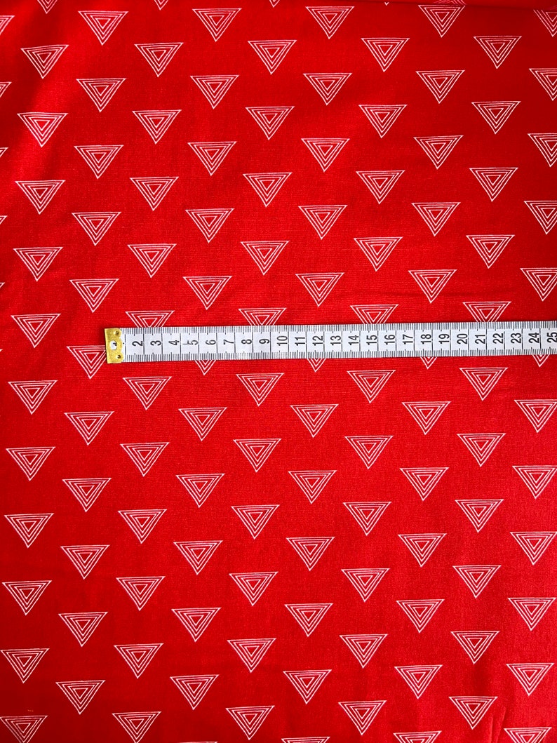 Może przedstawiać: Czerwona tkanina z powtarzającym się wzorem białych, zagnieżdżonych tr&oacute;jkąt&oacute;w. Taśma miernicza, oznaczona w centymetrach, jest ułożona na tkaninie. Odpowiednia do projekt&oacute;w krawieckich lub rękodzielniczych.