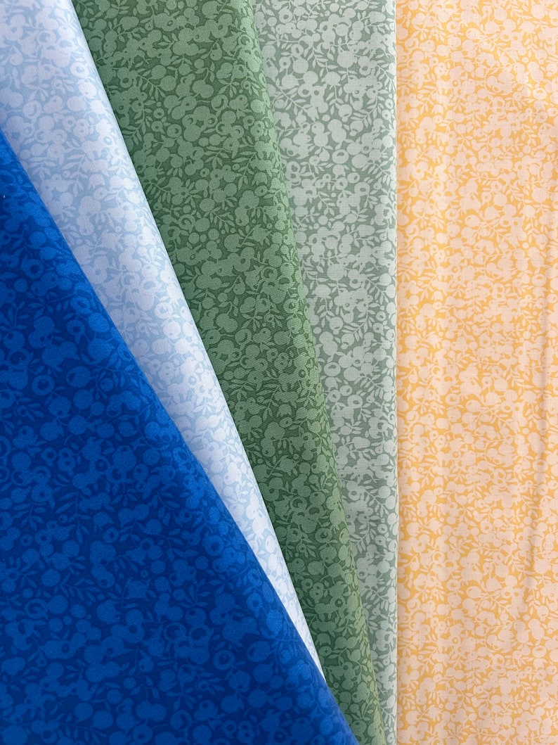 Pu&ograve; includere: Quattro campioni di tessuto con un motivo floreale bianco su sfondi di colori diversi. I campioni sono blu, verdi, blu chiaro e gialli.