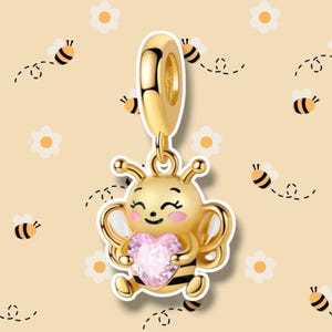 May include: A gold-colored bee charm with a pink heart-shaped gem. The bee has a smiling face, black stripes, and wings. The charm is designed to be a pendant or bead. The background features bees and flowers.