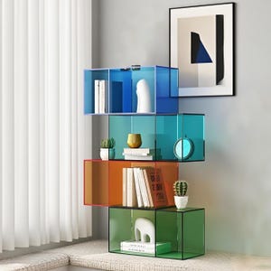 Puede incluir: Una pila de cuatro estanterías cúbicas de acrílico de colores azul, turquesa, naranja y verde. Cada estantería contiene objetos decorativos como libros, un reloj, un cactus y una escultura blanca. Una obra de arte abstracta enmarcada cuelga de la pared.